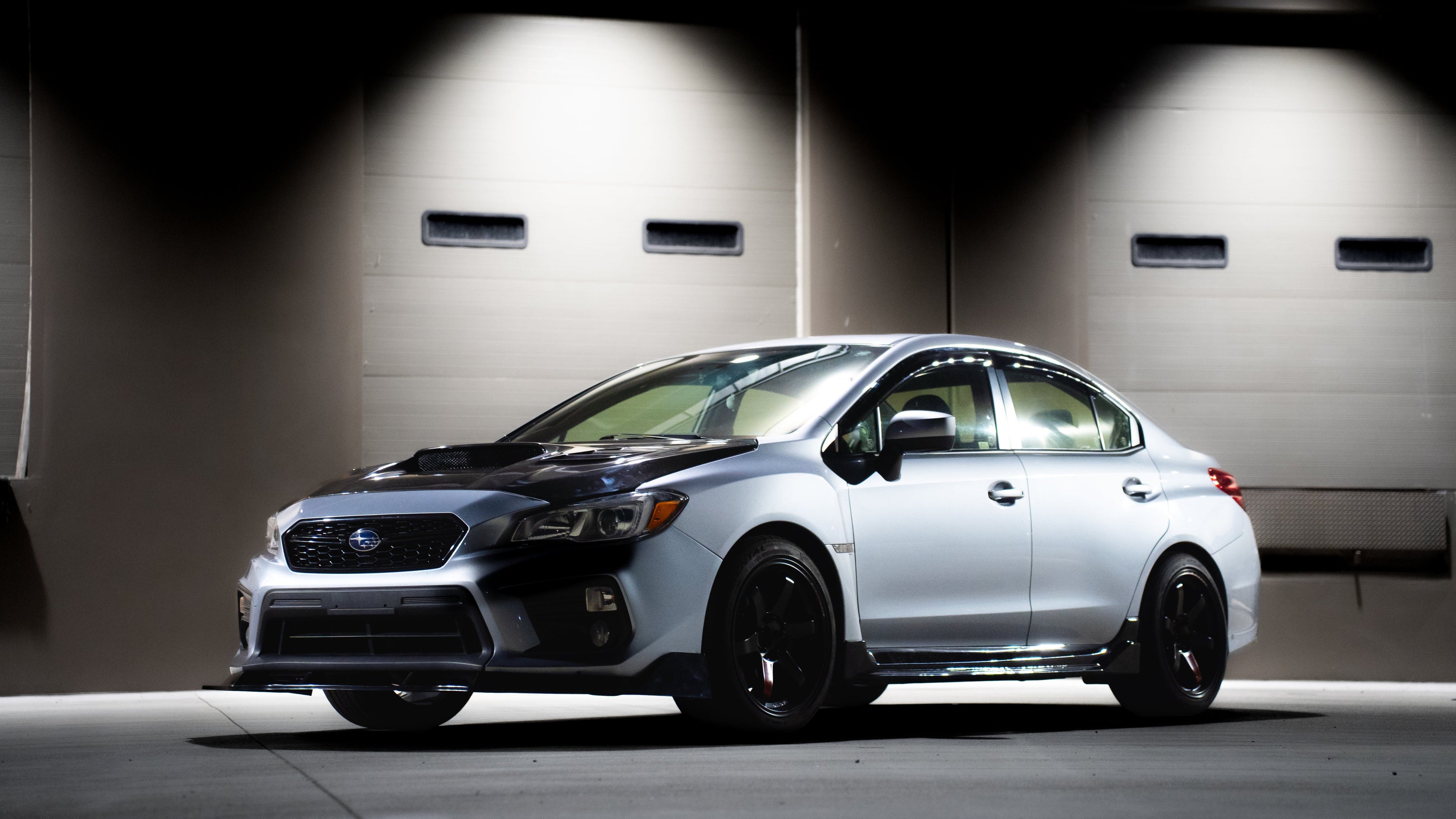 White car with black rims parked in a garage.